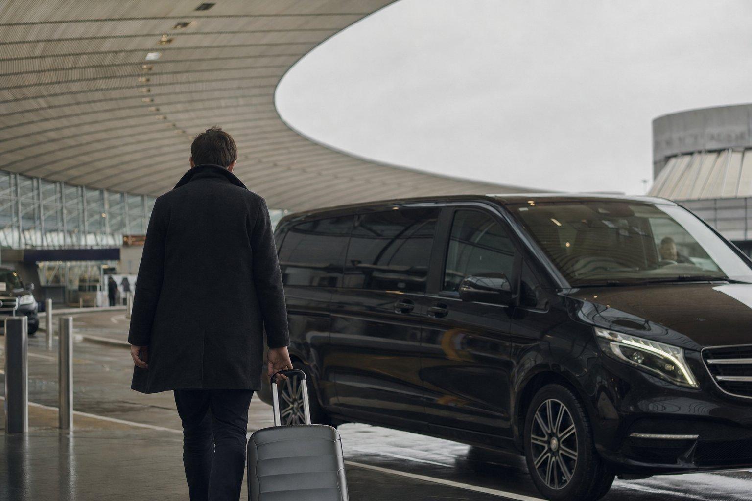 Voyageur seul de dos avec sa valise rejoignant un van noir Mercedes Classe V de navette privée au Terminal 2E de Roissy CDG, à la place des anciens Cars Air France vers Paris.