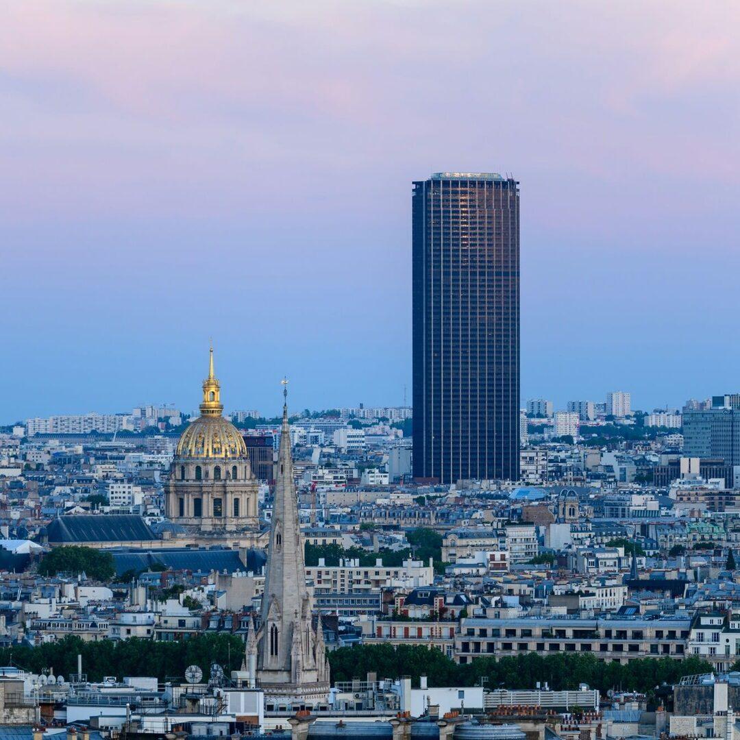 La Tour Montparnasse dominant les toits de Paris et le dôme des Invalides au coucher du soleil — destination de la navette privée Aéroparnasse depuis l’aéroport Roissy CDG.