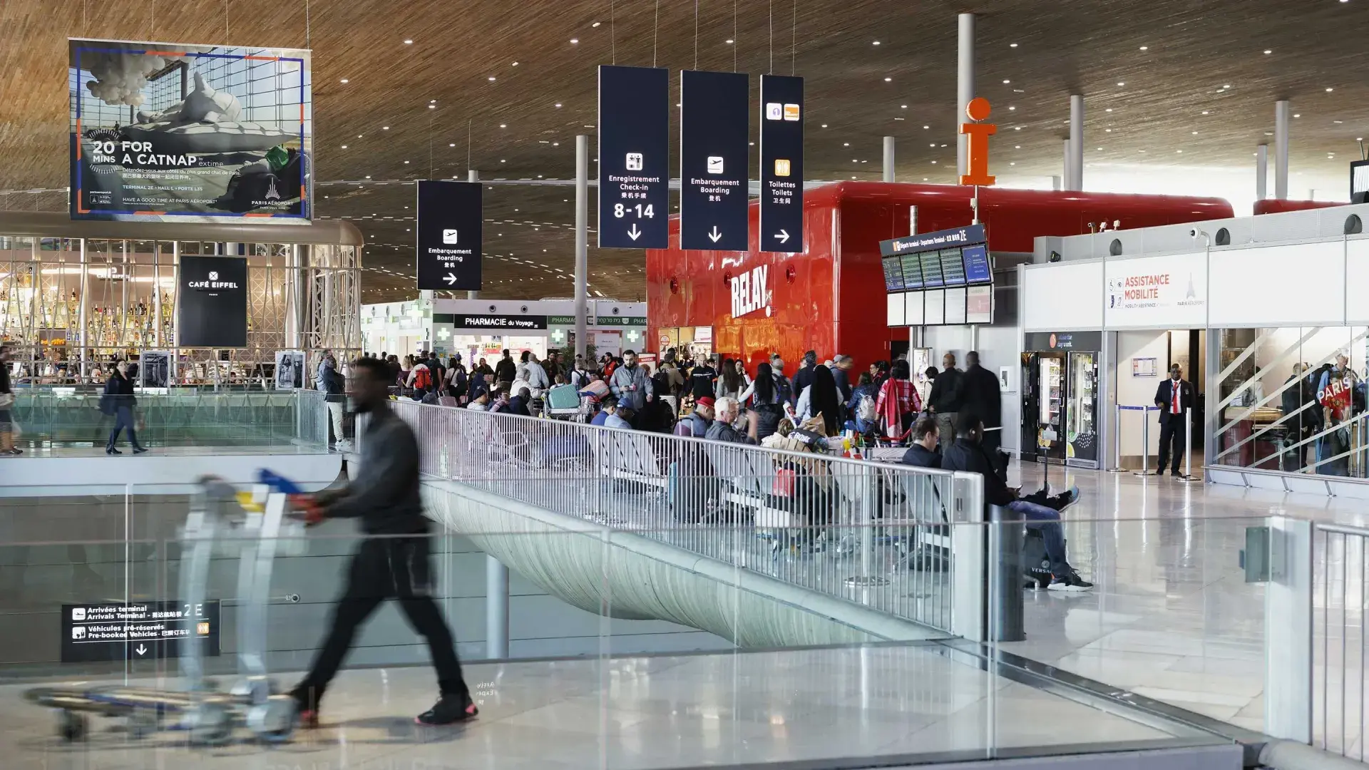 Le hall du Terminal 2E de l’aéroport Roissy-Charles-de-Gaulle, avec son plafond en bois courbe, ses panneaux et ses voyageurs.